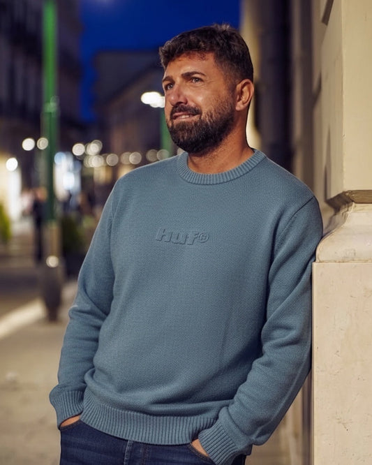 Manuel Store blue crewneck sweater with embossed HUF logo on chest, ribbed collar, cuffs, and hem.