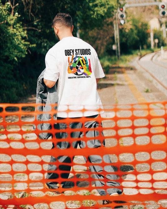 Manuel Store white 100% cotton t-shirt with colorful handprint graphic and "OBEY STUDIOS CREATIVE SERVICES DEPT." text.